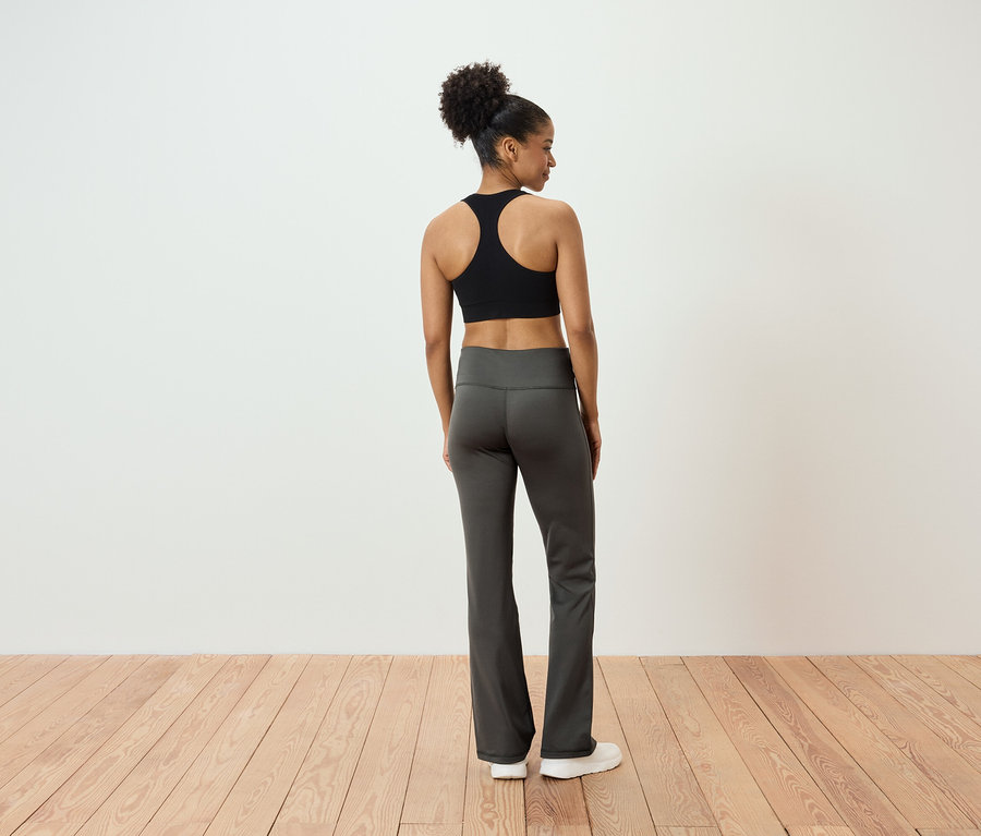 Z tyłu widać kobietę z włosami związanymi w koński ogon, ubraną w czarny biustonosz sportowy i szare spodnie.