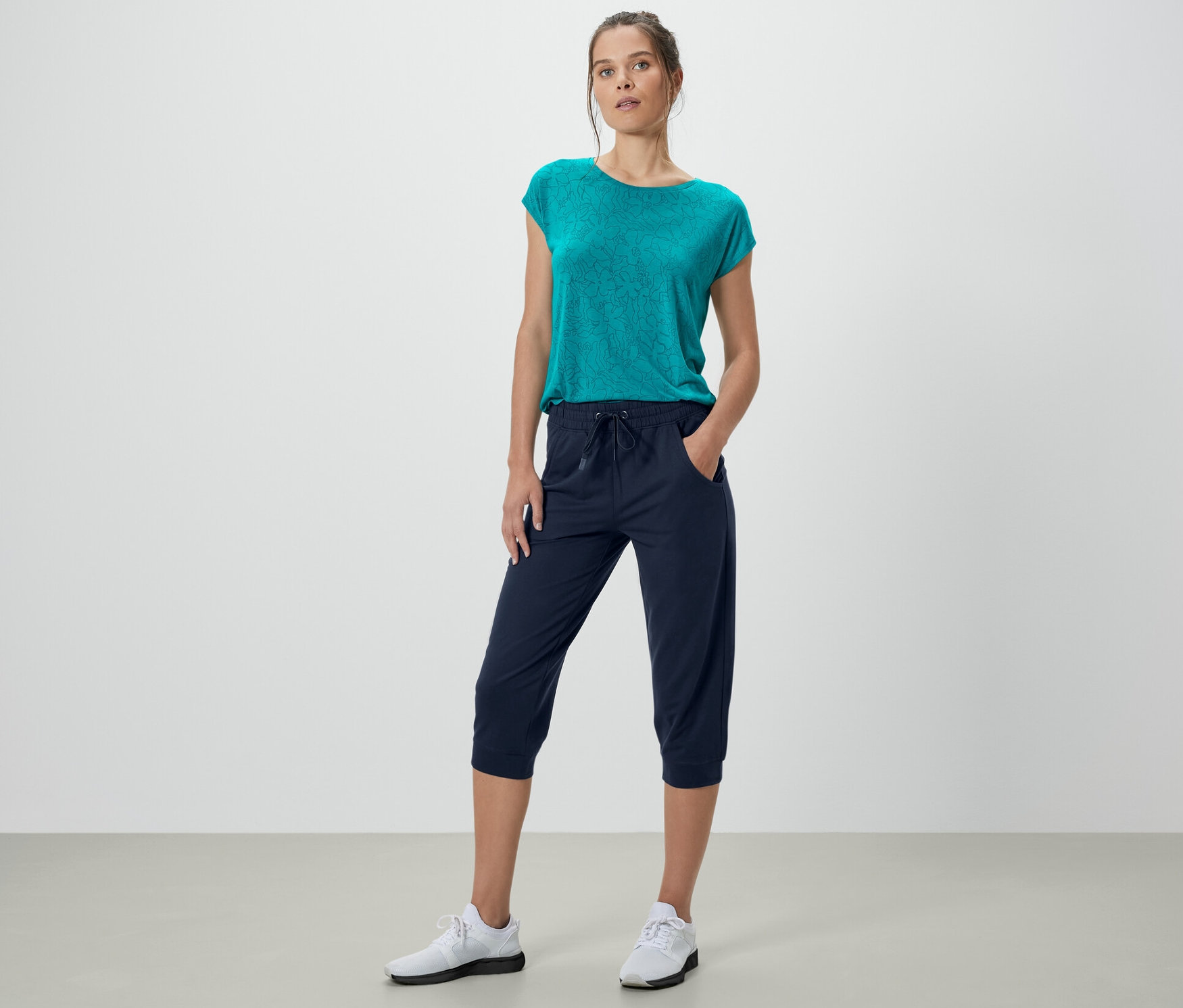 Kobieta pozuje w granatowych spodniach dresowych 3/4 i turkusowej bluzce.