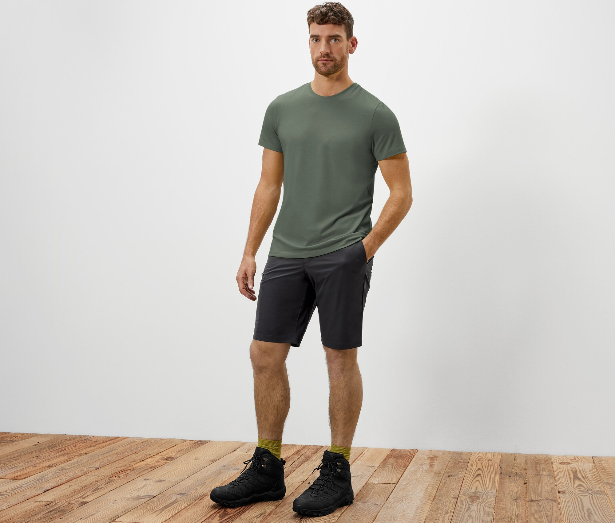 Mężczyzna stoi z ręką w kieszeni szortów funkcyjnych z softshellu.