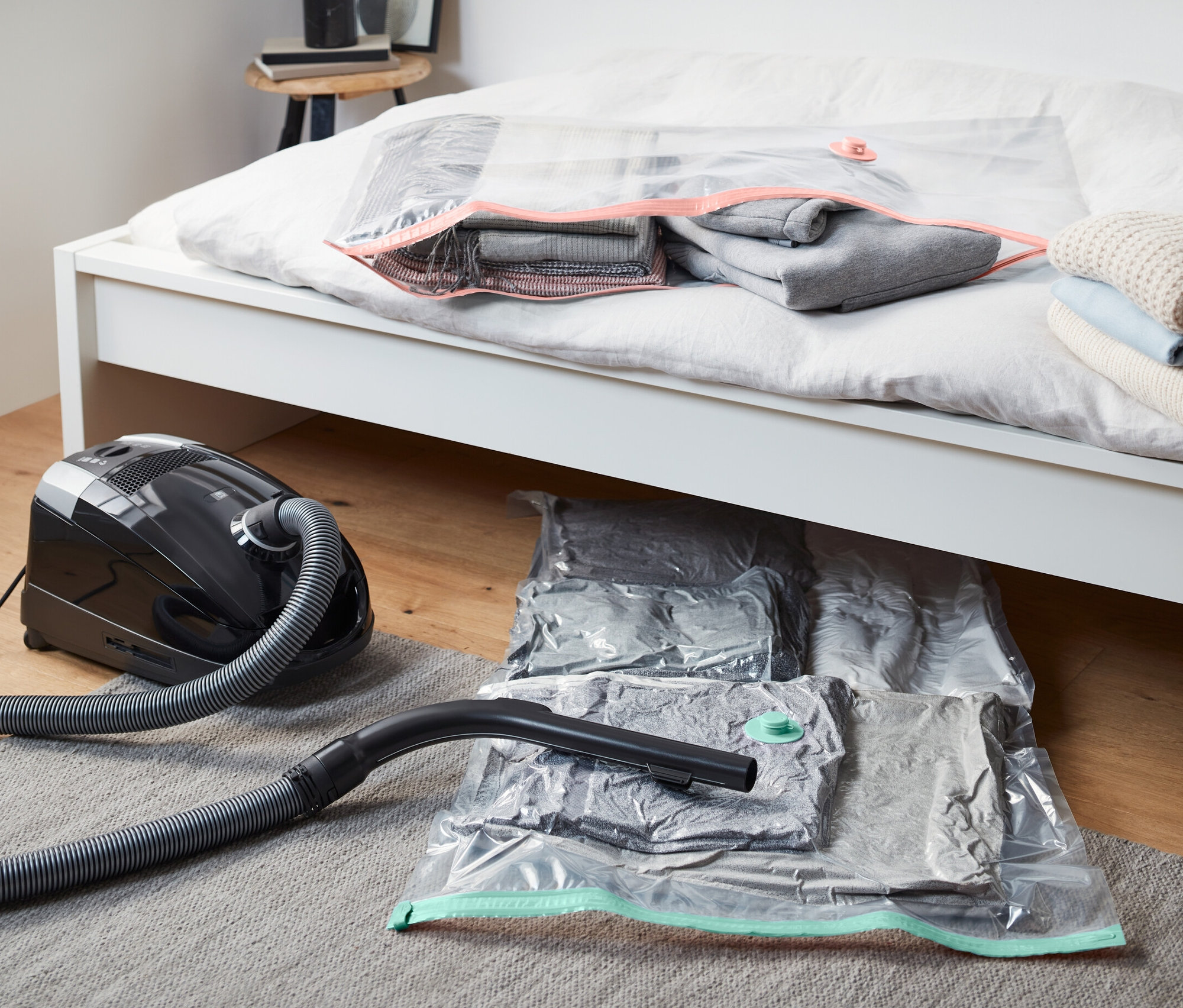 Odkurzacz leży obok dwóch worków próżniowych pod łóżkiem. Jeden worek próżniowy leży na łóżku.