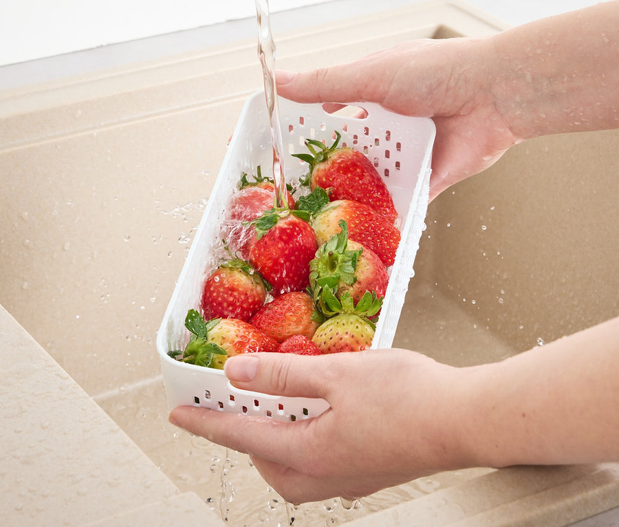 Osoba myje truskawki w zlewie w pojemniku spożywczym z sitkiem.