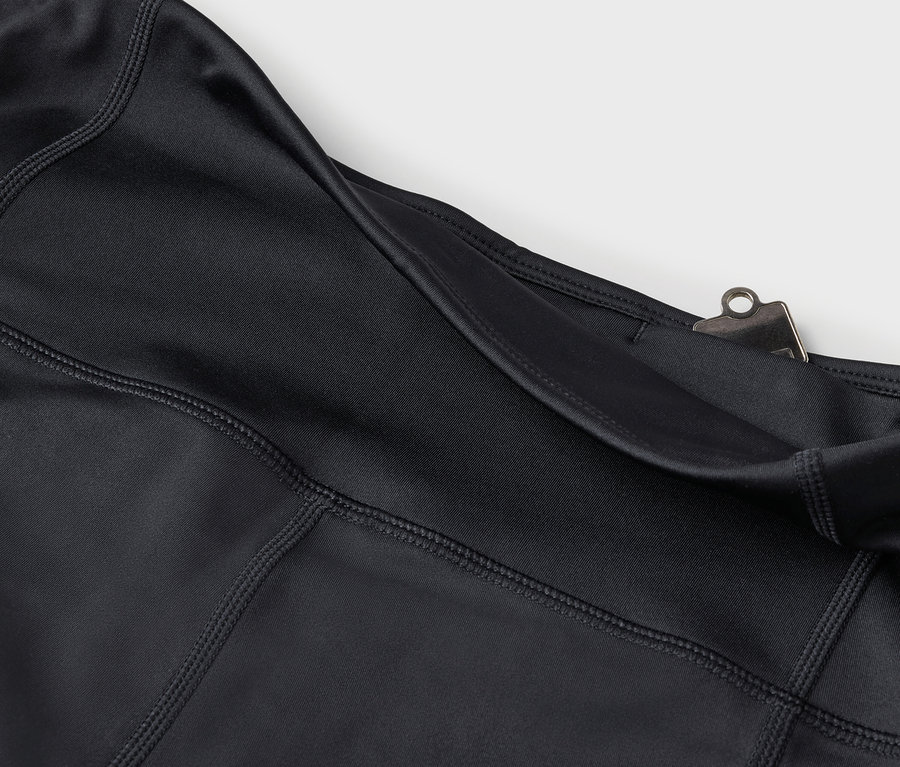 Szczegół czarnych legginsów z kieszenią i srebrnym klipsem.