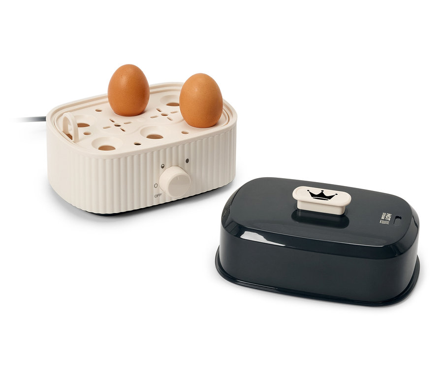 Dwa brązowe jajka na kremowym elektrycznym urządzeniu do gotowania jajek obok czarnej pokrywki.