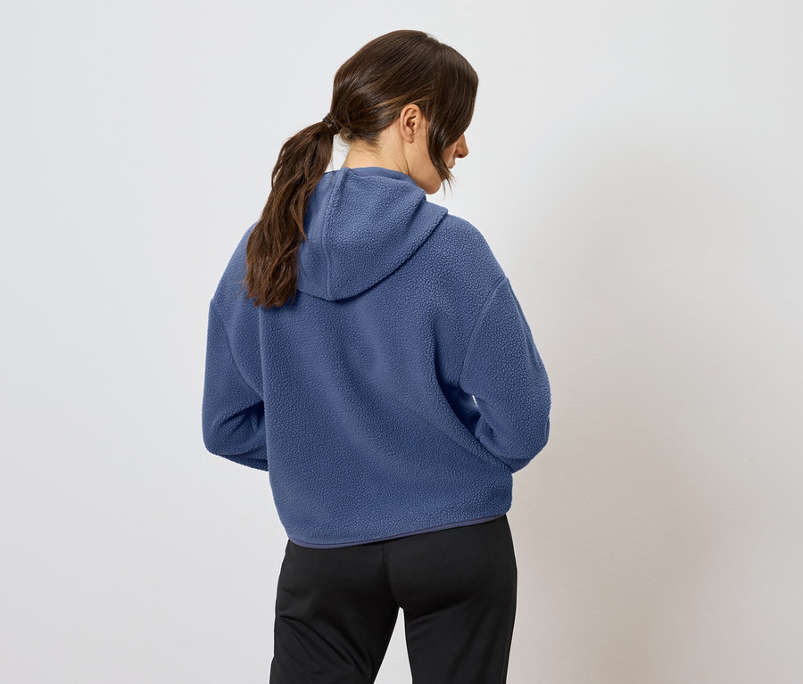 Widok z tyłu kobiety z brązowymi włosami związanymi w kucyk, ubranej w niebieską bluzę z kapturem i czarne spodnie.