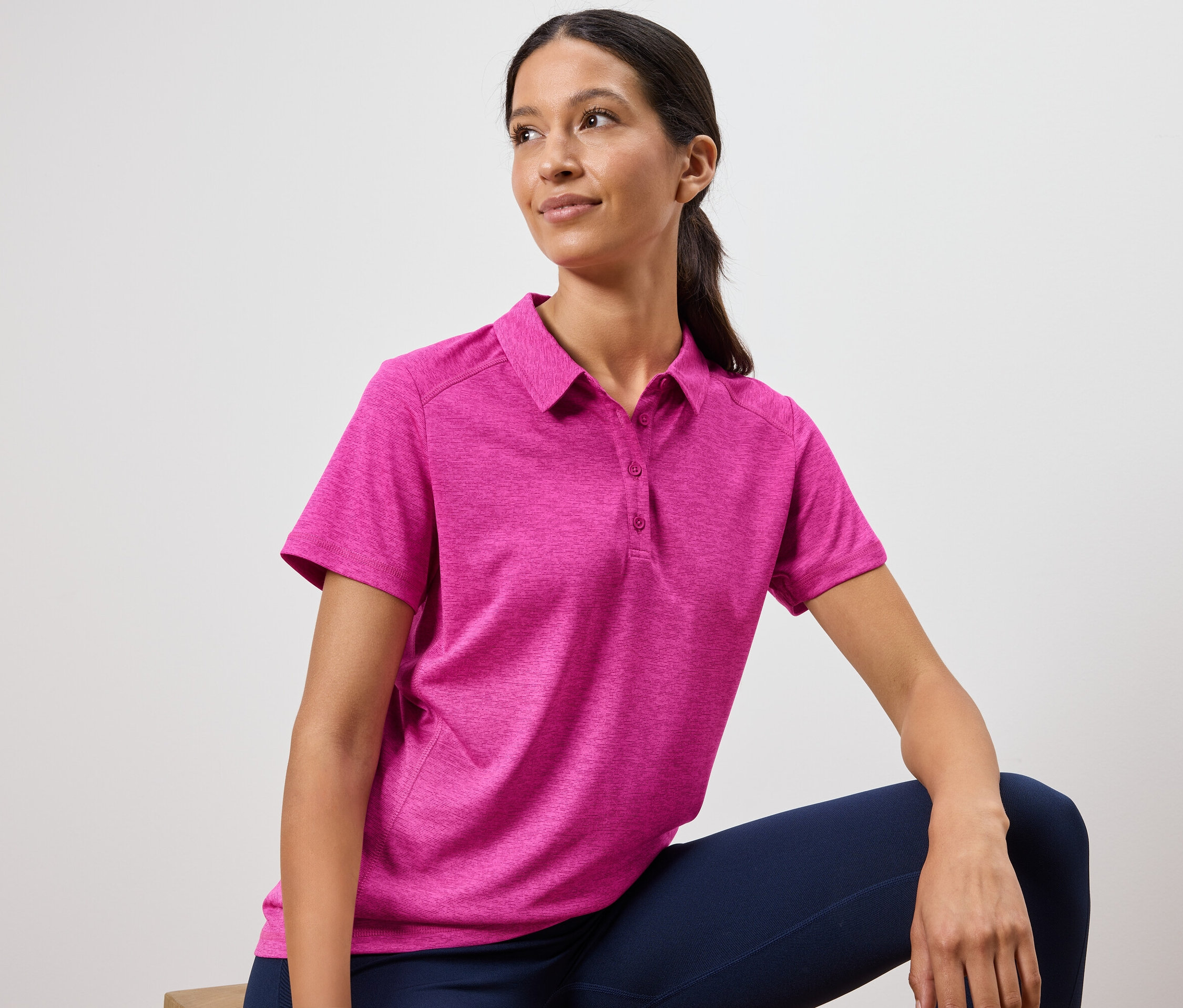Kobieta ma na sobie różową koszulkę polo i granatowe legginsy.