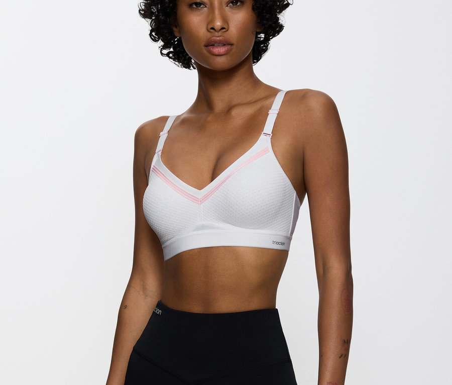 Kobieta ma na sobie biały biustonosz sportowy z różowymi detalami i czarne legginsy.