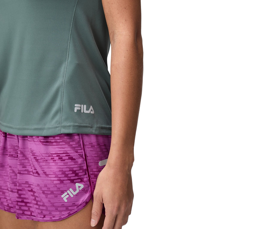 Zbliżenie kobiety w zielonym topie Fila i fioletowych szortach.