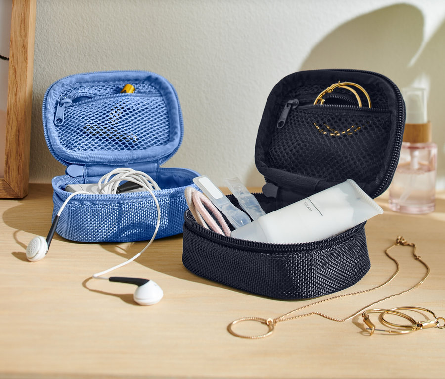 Na stole stoją dwie otwarte, małe torby do przechowywania, jedna niebieska ze słuchawkami, a druga ciemna z produktami do pielęgnacji skóry i biżuterią.