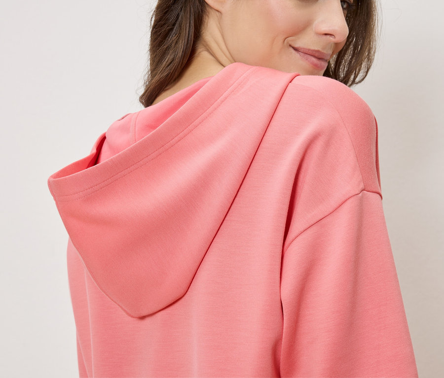 Kobieta ma na sobie łososiową bluzę z kapturem, widziana z boku.