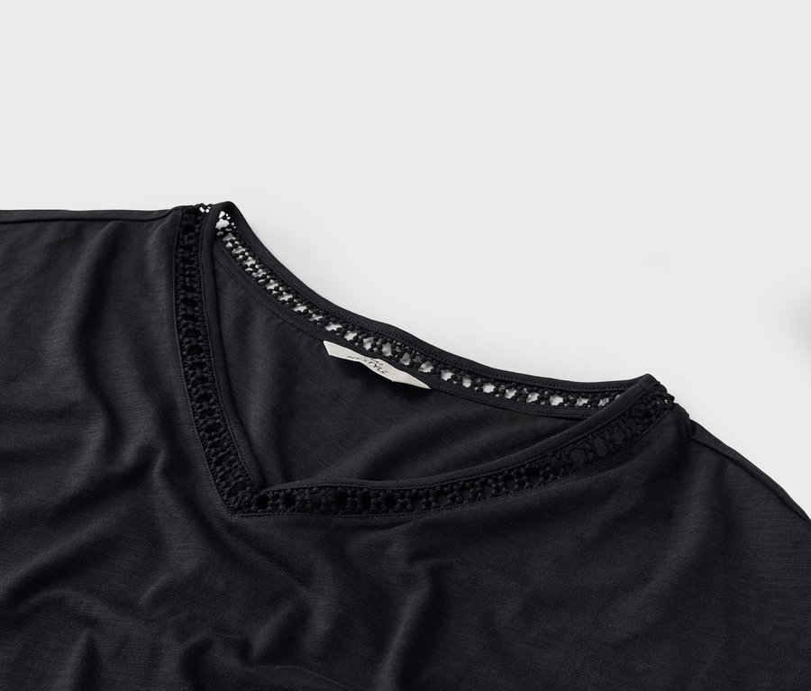 Zbliżenie czarnego T-shirtu z dekoltem w serek i koronkowymi detalami przy dekolcie.
