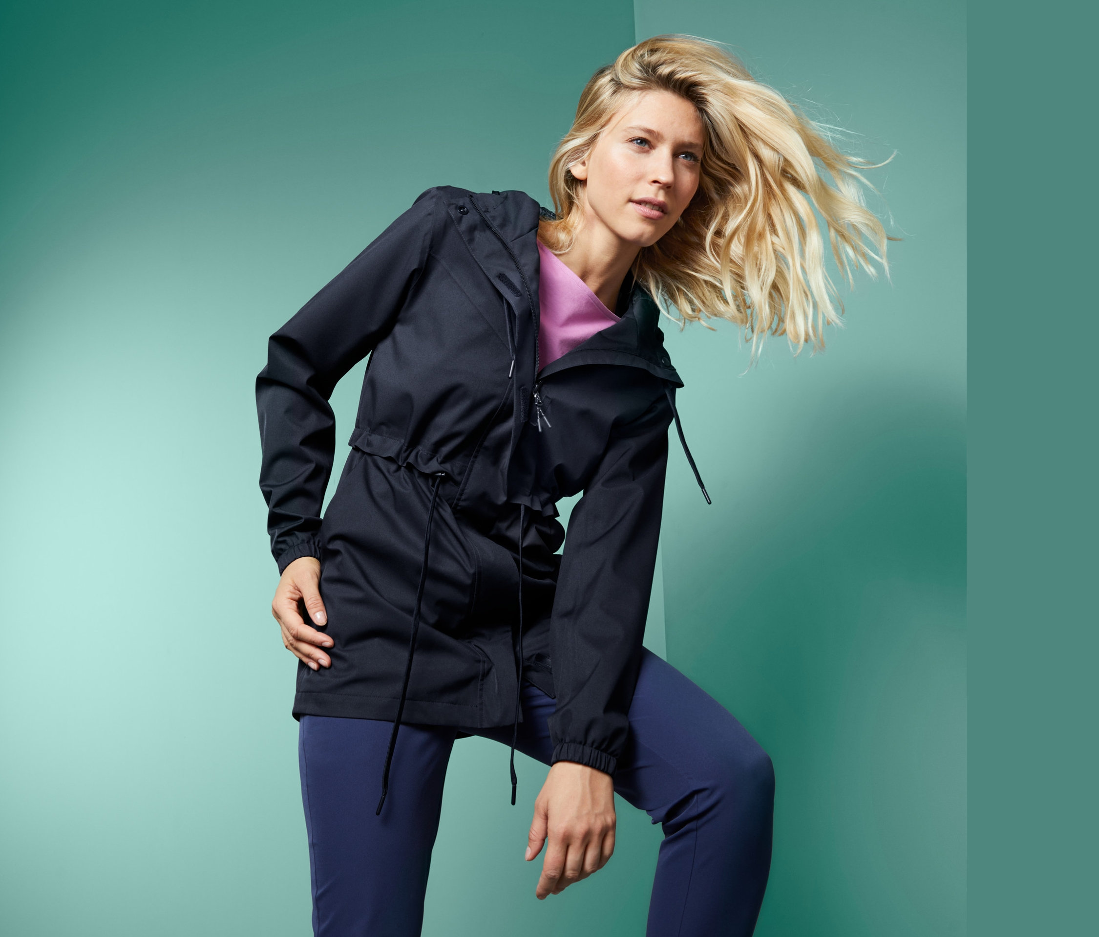 Kobieta pozuje w granatowej kurtce przeciwdeszczowej ze ściągaczem w pasie i kapturem.