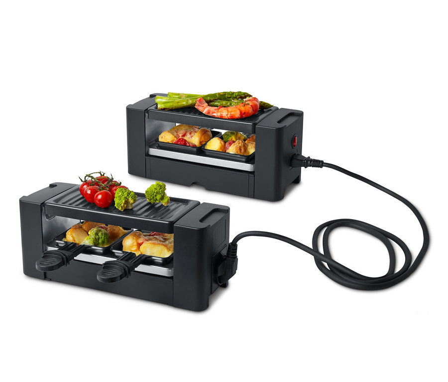 Dwa czarne grille raclette dla dwóch osób z różnymi potrawami na górze i w środku.