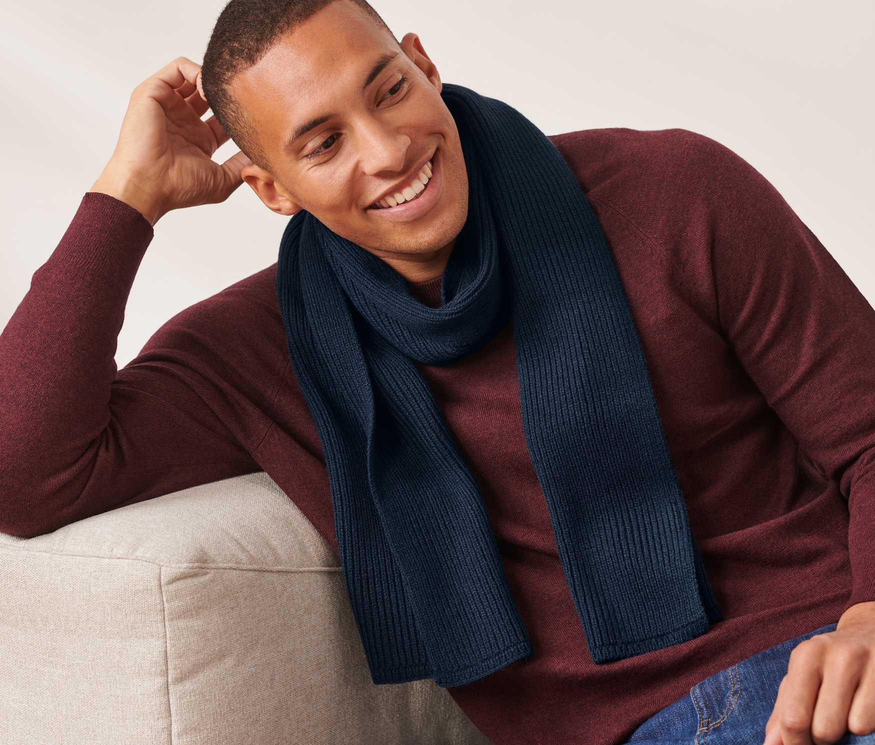 Mężczyzna siedzi na kanapie i ma na sobie niebieski szal z dzianiny.