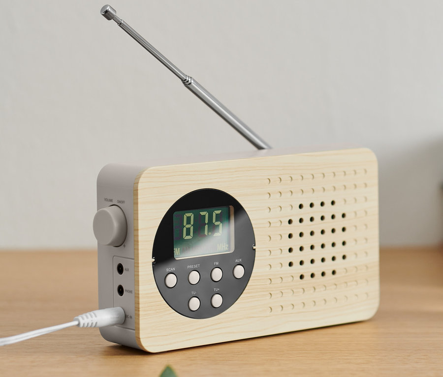Kompaktowe radio FM z wysuwaną anteną stoi na drewnianej szafce.