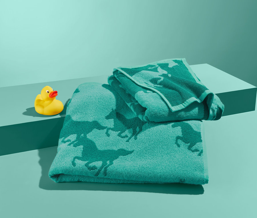 Zestaw ręczników z motywem koni i żółta gumowa kaczka na turkusowym tle.