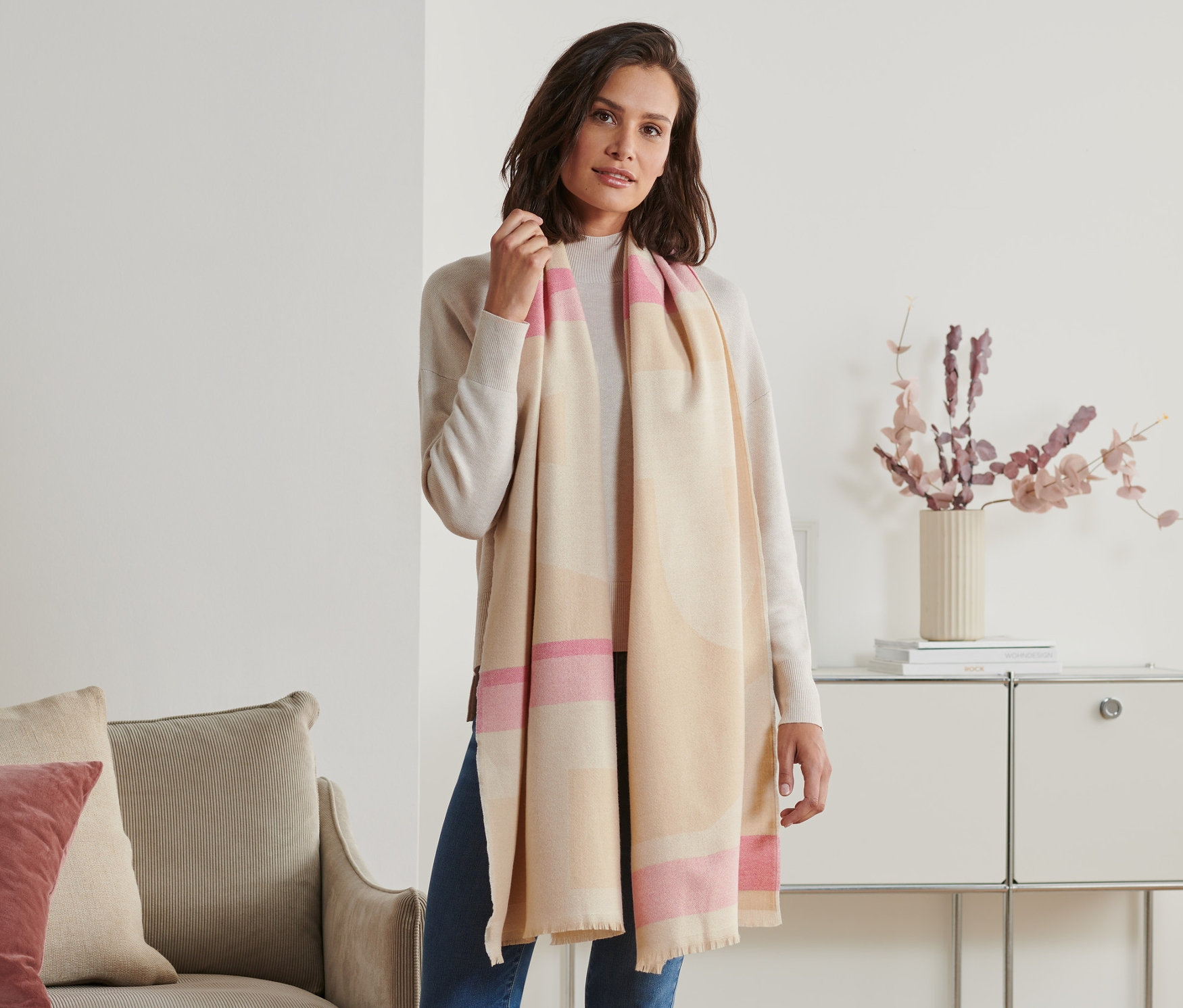 Kobieta pozuje w beżowo-różowym szalu z frędzlami.