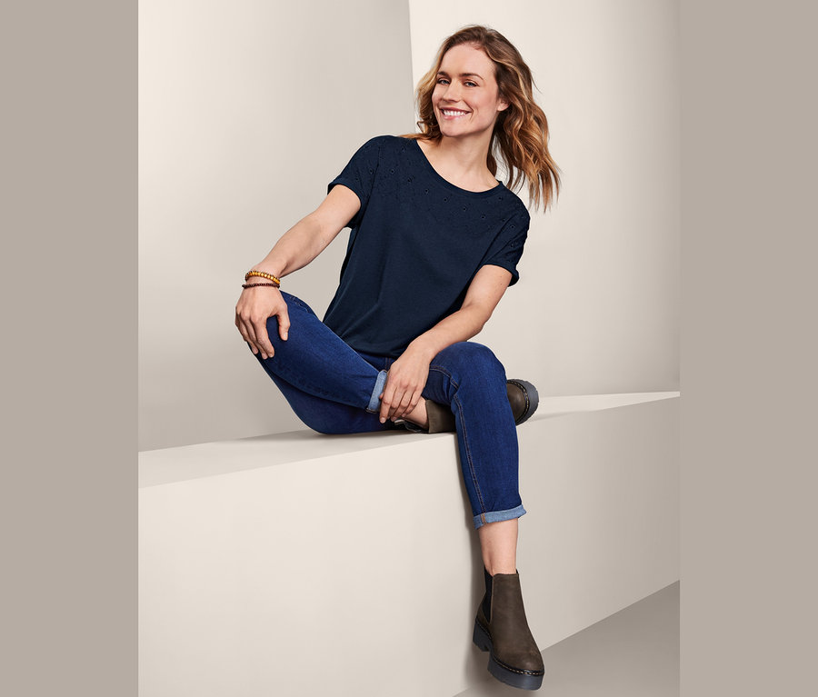 Kobieta siedzi w niebieskich dżinsach i damskiej koszulce z krótkimi rękawami z haftem.