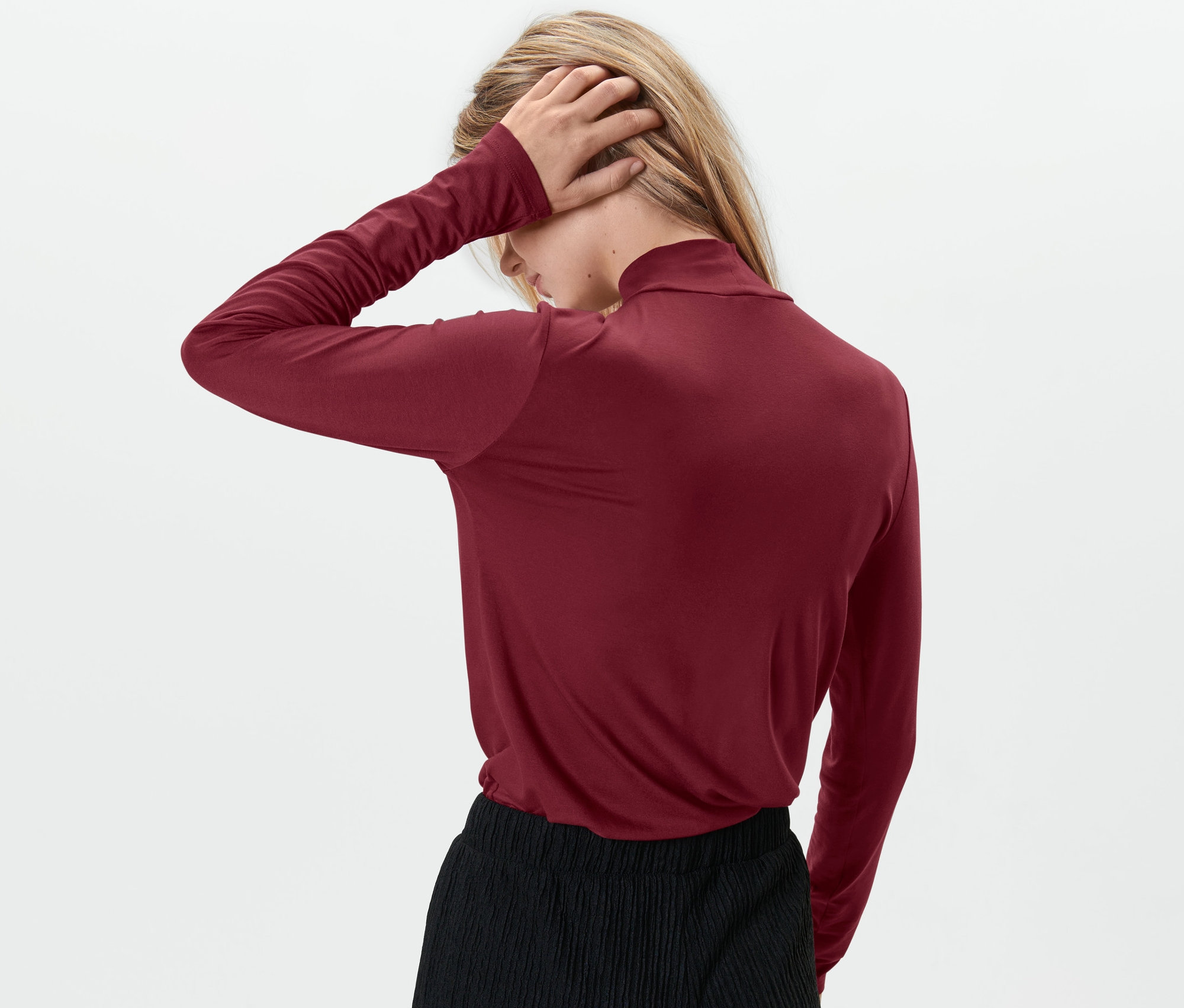 Kobieta ma na sobie czerwoną bluzkę ze stójką i czarne spodnie.