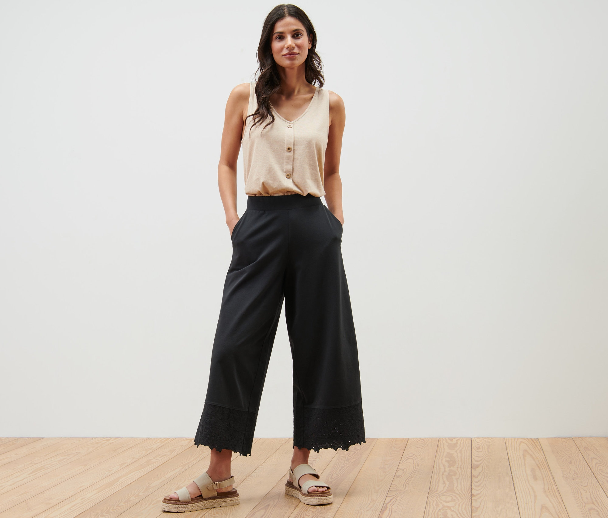 Kobieta pozuje w beżowym topie i czarnych kulotach z haftem.