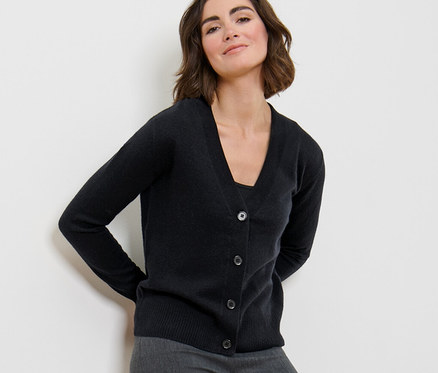 Kobieta pozuje w czarnym kardiganie z delikatnej dzianiny z kaszmirem i szarych spodniach.