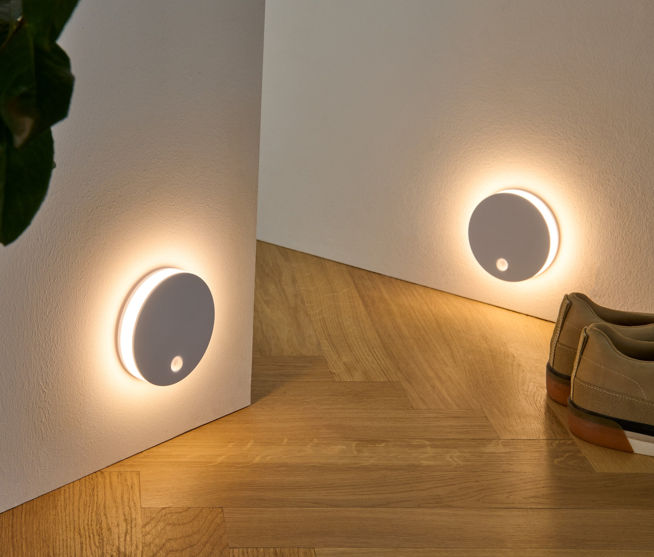 Dwie wielofunkcyjne lampki LED przymocowane do ściany, wraz z rośliną w wiklinowym koszu i butami na drewnianej podłodze.