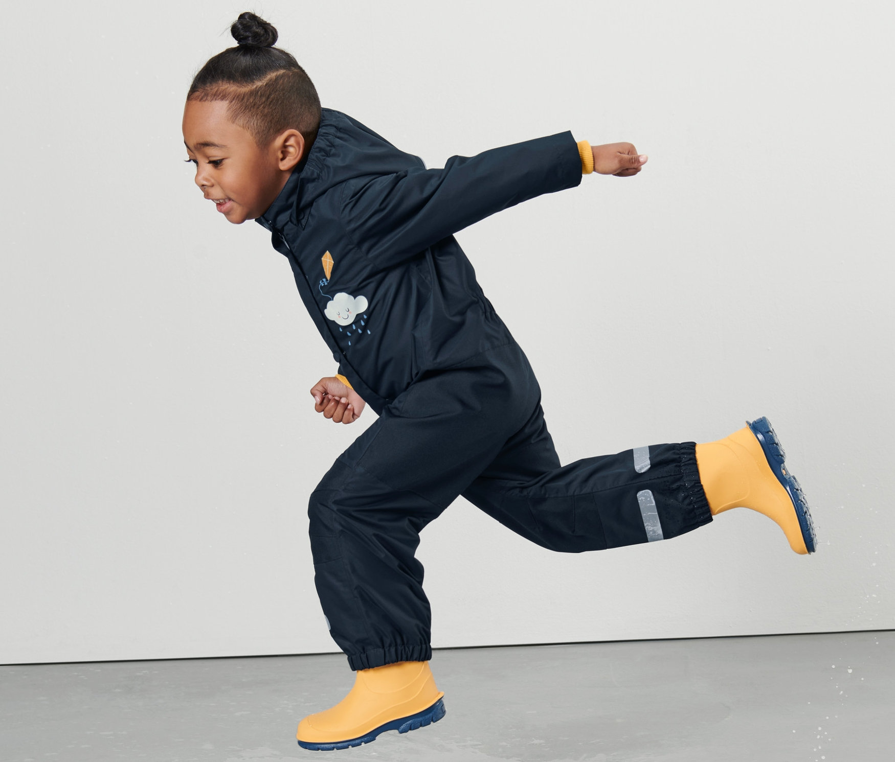 Chłopiec w kombinezonie przeciwdeszczowym skacze w kałuży.