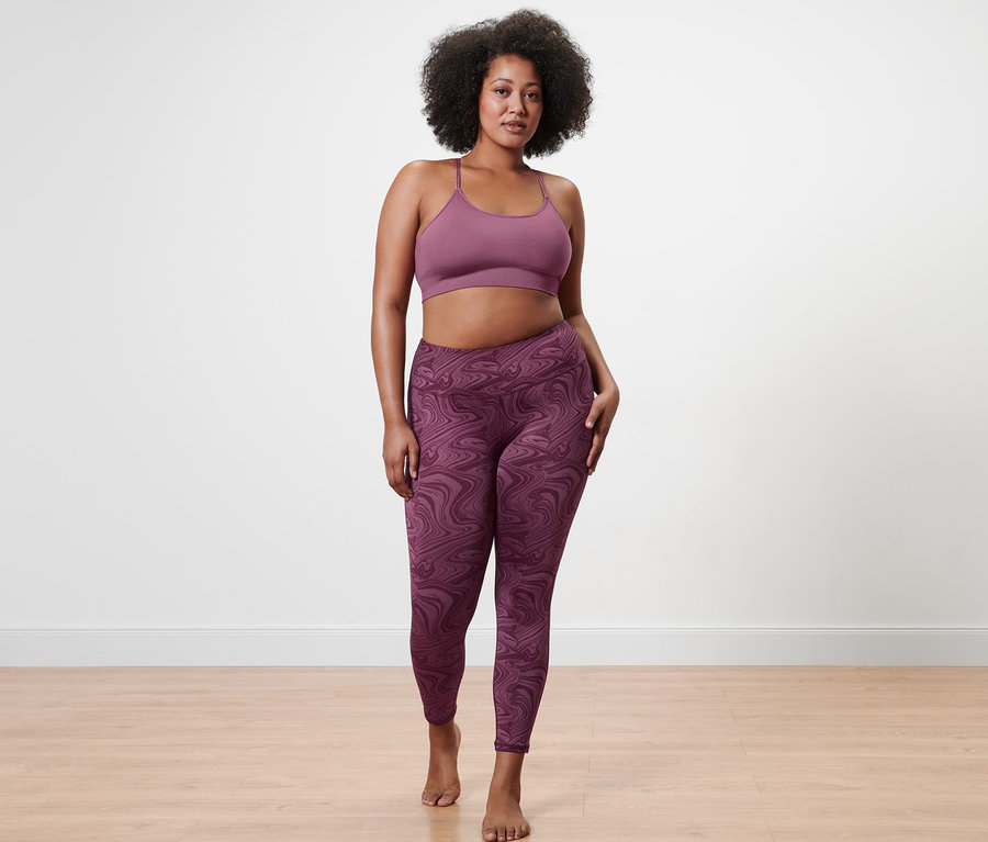 Kobieta pozuje w bezszwowym biustonoszu sportowym i legginsach sportowych o długości 7/8.