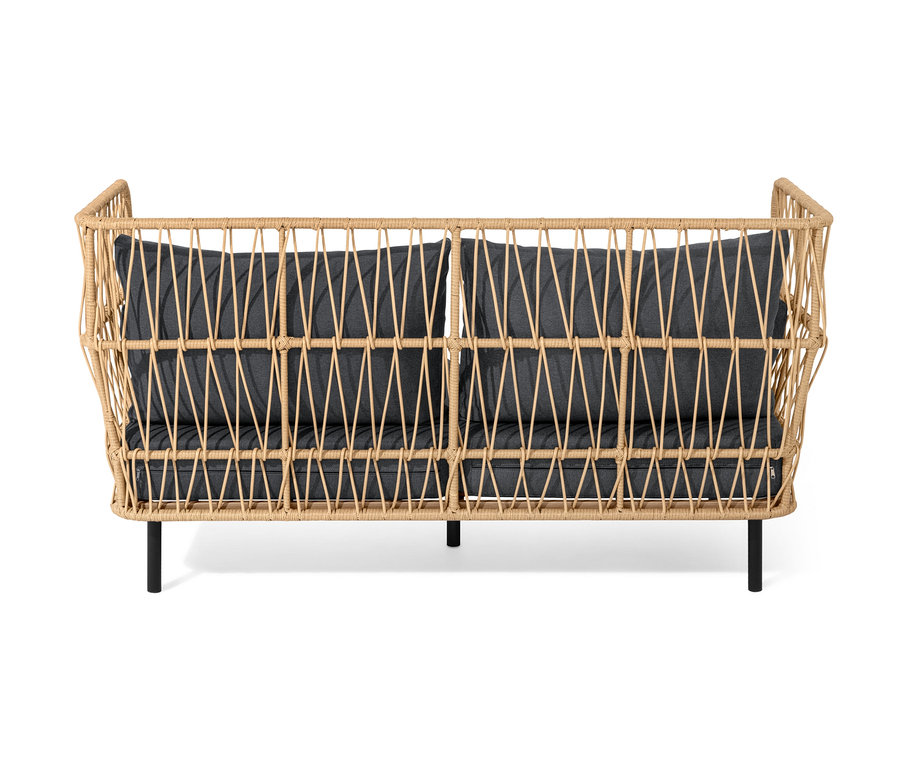 Wiklinowa sofa z podnóżkiem i ciemnoszarymi poduszkami.