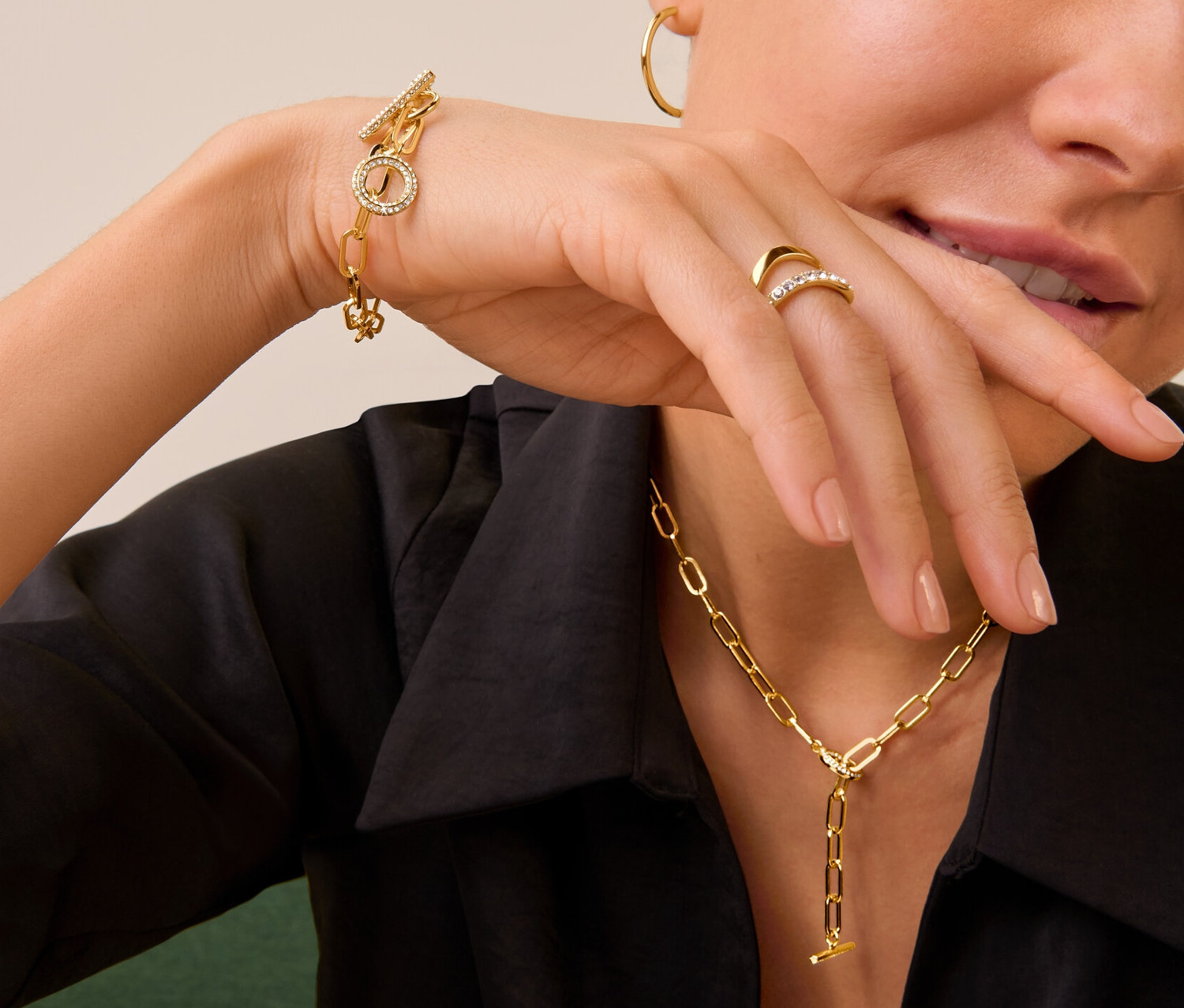 Kobieta nosi złoty pierścionek z podwójną falą i kamieniami, naszyjnik i bransoletkę Toggle osadzane kamieniami oraz złote kolczyki koła.