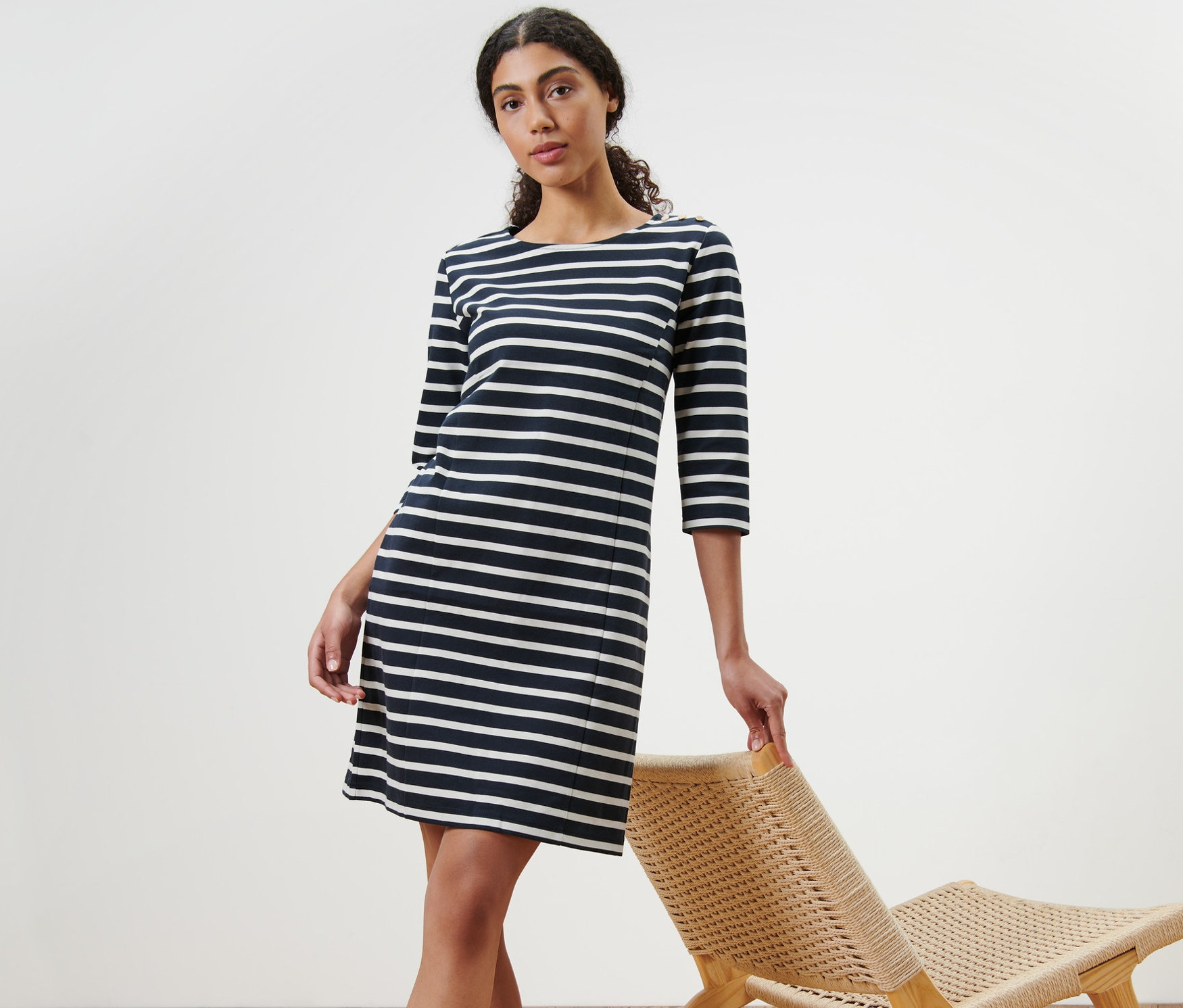 Kobieta pozuje w sukience z dzianiny dresowej w paski obok wiklinowego krzesła.