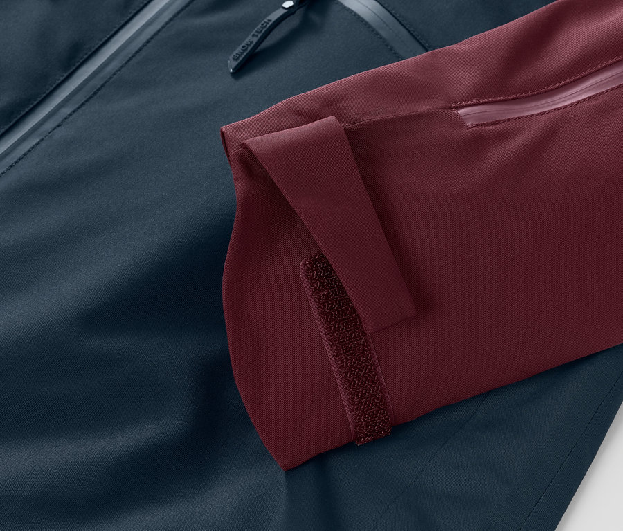 Zbliżenie kurtki narciarskiej i snowbordowej: bordowy rękaw z regulowanym mankietem na rzep i granatowa reszta kurtki.