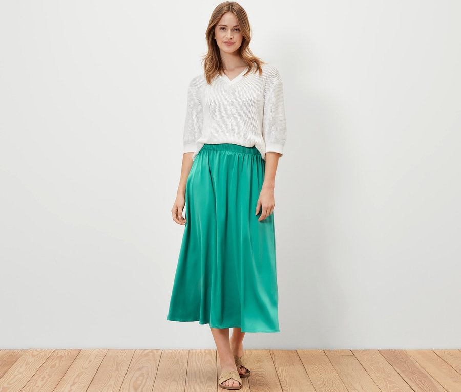 Kobieta pozuje w białym topie i zielonej spódnicy z satyny.
