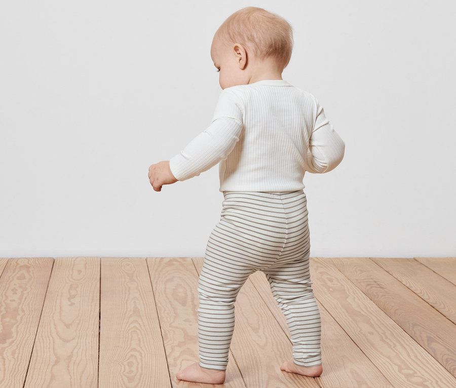 Małe dziecko chodzi po drewnianej podłodze, ubrane w legginsy dziecięce w paski, 5 par.