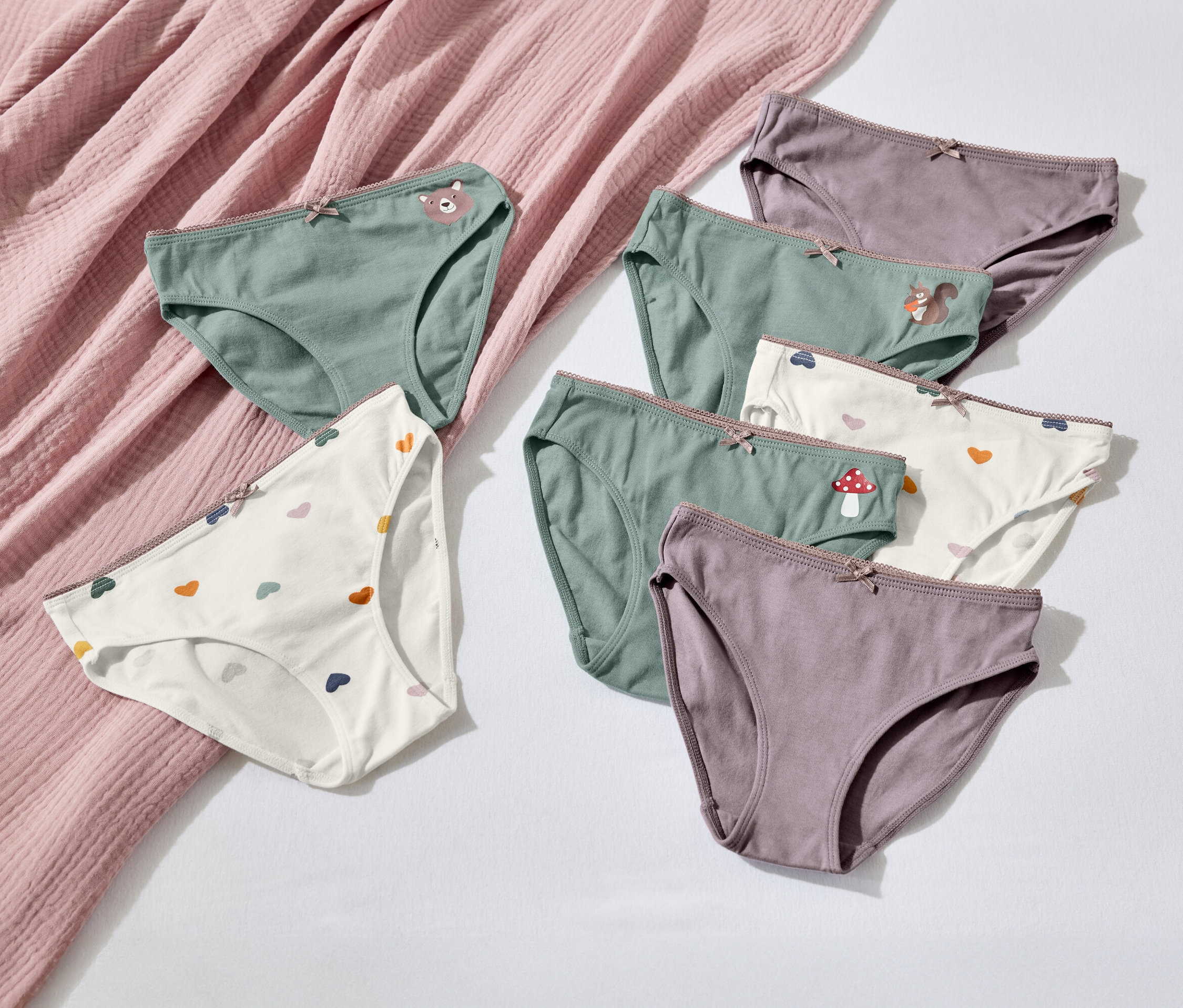 Siedem par damskiej bielizny w różnych kolorach i wzorach leży na białym tle obok różowej tkaniny.