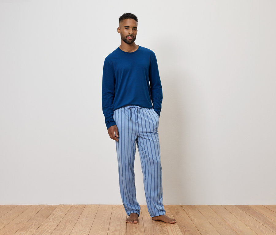 Mężczyzna w niebieskiej piżamie z długim rękawem i spodniach w paski.