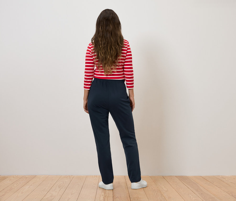 Kobieta w bluzce w paski czerwono-białe i granatowych spodniach stoi tyłem do aparatu.
