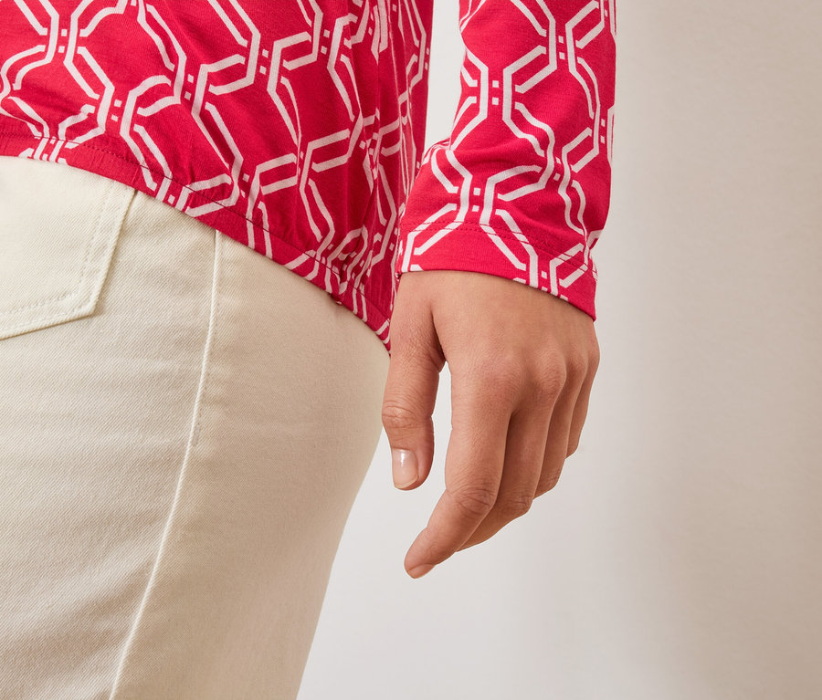 Zbliżenie na dłoń kobiety, czerwono-białą bluzkę i jasne spodnie.