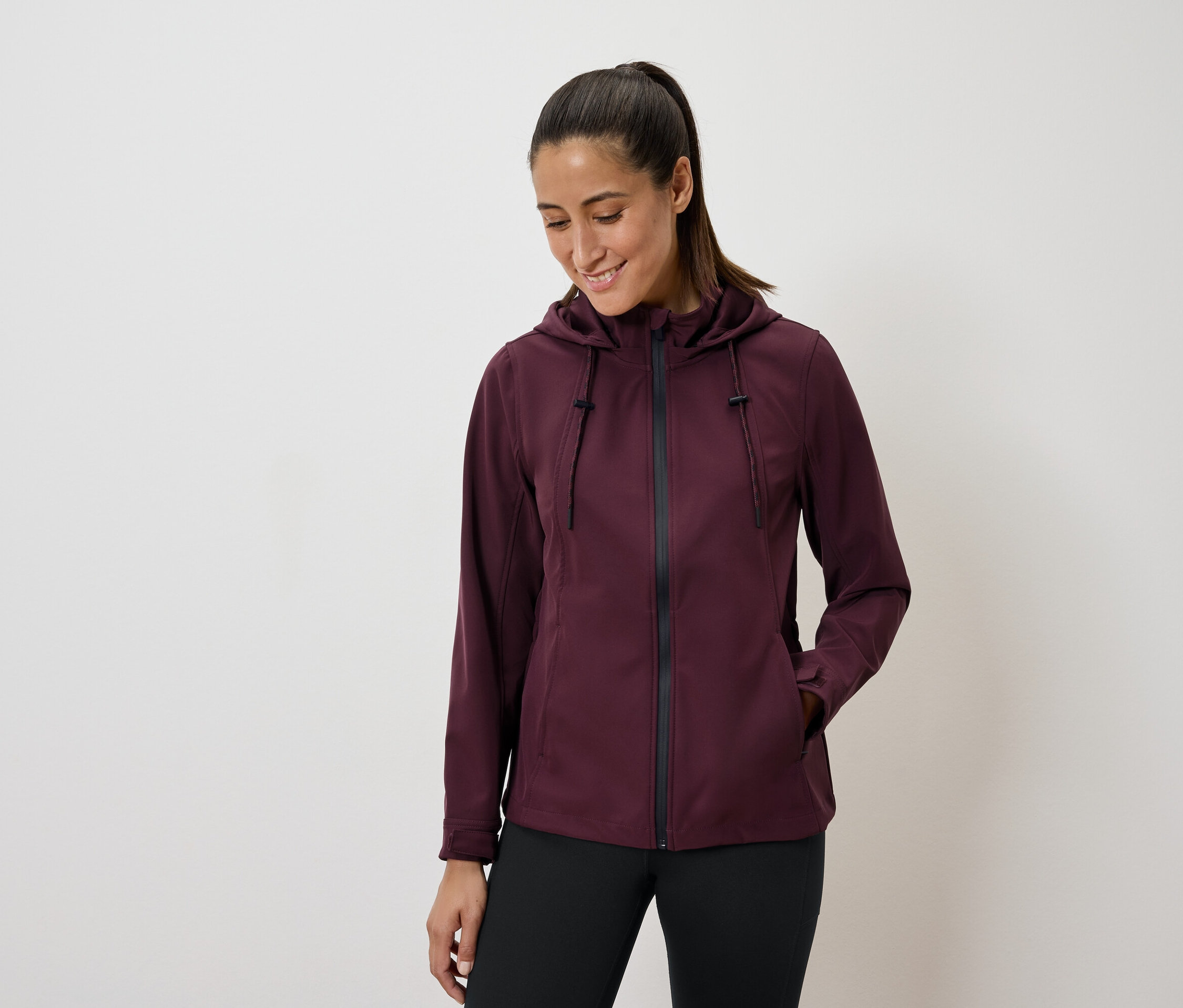 Kobieta w bordowej kurtce z kapturem i czarnych legginsach.