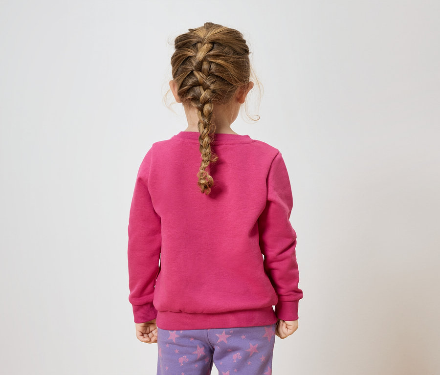 Dziewczynka w warkoczu stoi tyłem, ubrana w różową bluzę i fioletowe spodnie w gwiazdy.