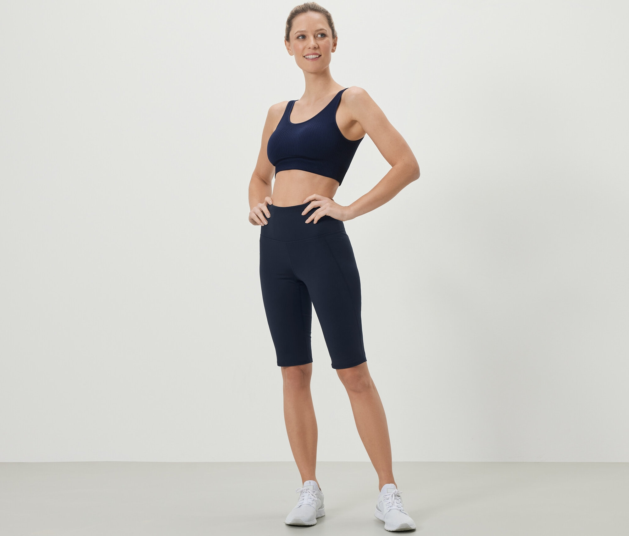 Kobieta pozuje w granatowym staniku sportowym i krótkich legginsach.