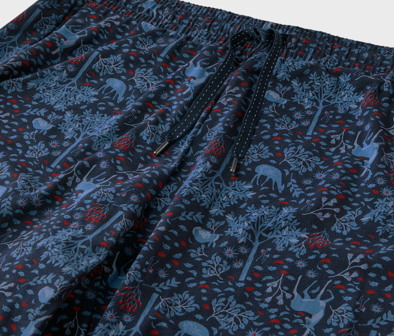 Szczegółowe ujęcie niebieskich spodni z wzorem lasu, drzew i jeleni.
