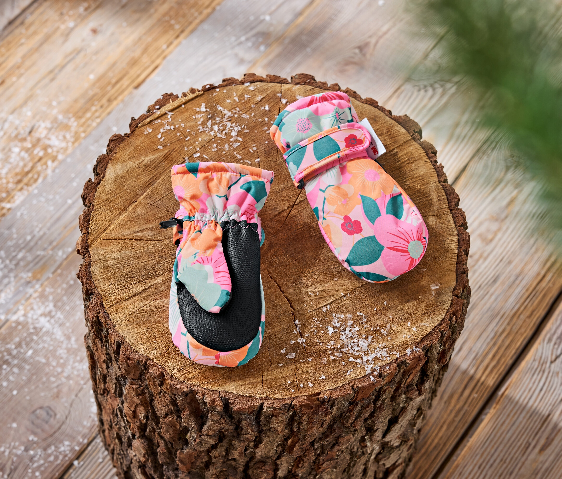 Dziecięce rękawice z kwiatowym wzorem leżą na drewnianym klocku.
