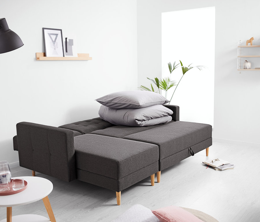 Sofa narożna sprężynowa ze skrzynią stoi w salonie.