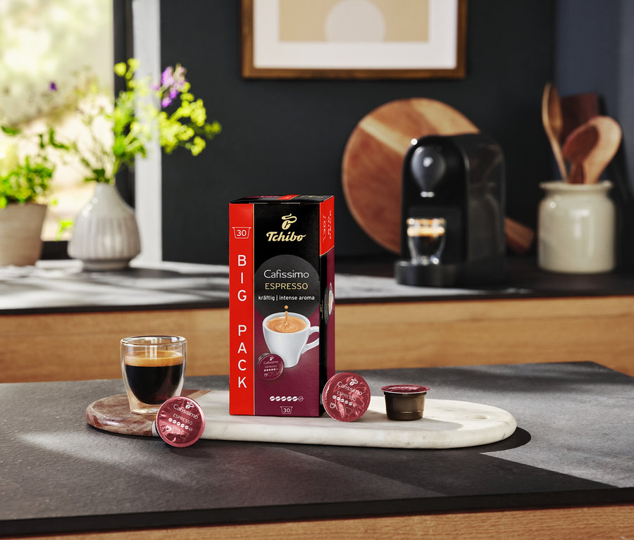 Szklanka do espresso stoi obok opakowania Cafissimo Espresso i kapsułek na marmurowej tacy.