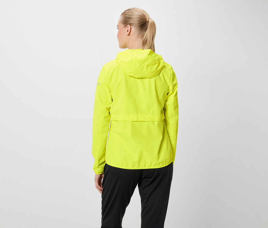 Z tyłu widać kobietę z blond włosami związanymi w kucyk, ubraną w neonowo żółtą kurtkę z kapturem i czarne spodnie.