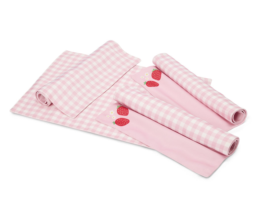 Na białym tle leży różowo-biały koc w kratę i dwie różowe tkaniny z motywami truskawek, częściowo zwinięte.