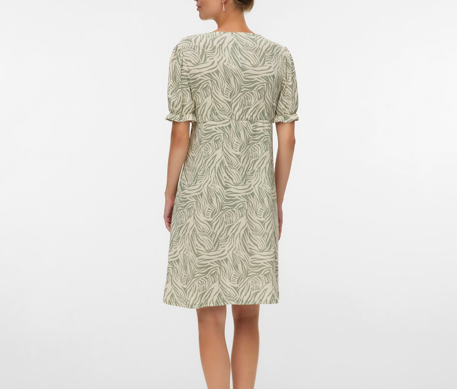 Kobieta widziana od tyłu w sukience do kolan w zebrę i sandałach.