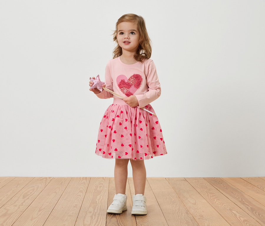 Mała blondynka w różowej sukience w serduszka trzyma różdżkę.