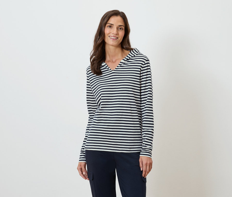 Kobieta ma na sobie bluzkę w paski z długim rękawem i kapturem oraz granatowe spodnie.