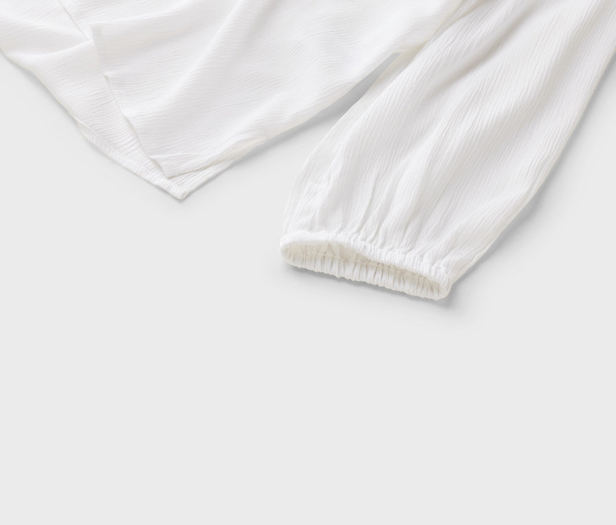 Szczegółowy widok białej bluzki z długimi rękawami i marszczonymi mankietami na białym tle.